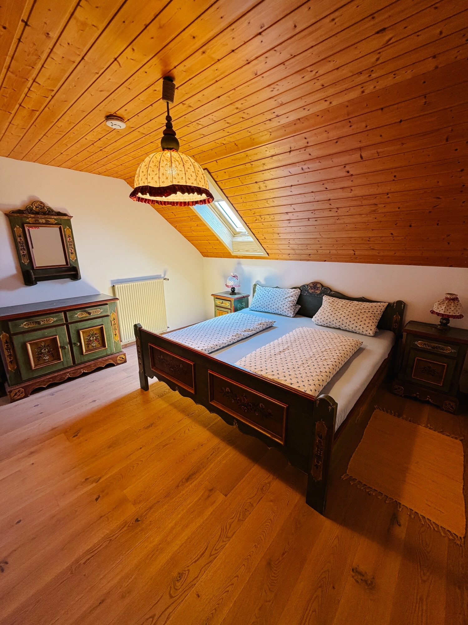 Schlafzimmer mit bemaltem Bauernbett, Holzdecke und traditionellen Nachttischen